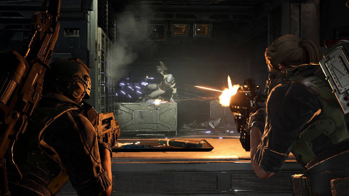 A dramatic sci-fi action scene showing two heavily armored soldiers aiming weapons toward a central figure in a smoky industrial interior, with bright muzzle flashes and glowing orange light.
