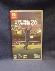 Nintendo Switch game case for Football Manager 26 Touch, featuring a cover with a football stadium scene and a coach raising his hand, photographed against a dark textured fabric background.