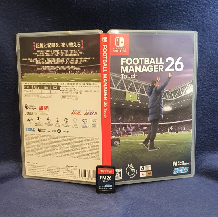 Nintendo Switch version of Football Manager 26 Touch game case shown open to display the front cover, back menu, and spine, with a small FM26 storage card in front, photographed on a blue textured fabric background.