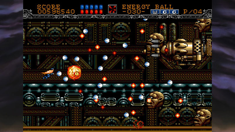 A screenshot of a retro 2D video game scene with a side-scrolled platformer layout. The frame shows a small orange character on the left, glowing orange energy balls, metallic gold and dark blue machinery, and a score/health/level header at the top.