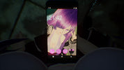 A black smartphone held in a dark environment, displaying a pink anime wallpaper with a purple-haired character. The phone is centered, with blurred dark shapes in the foreground and background.