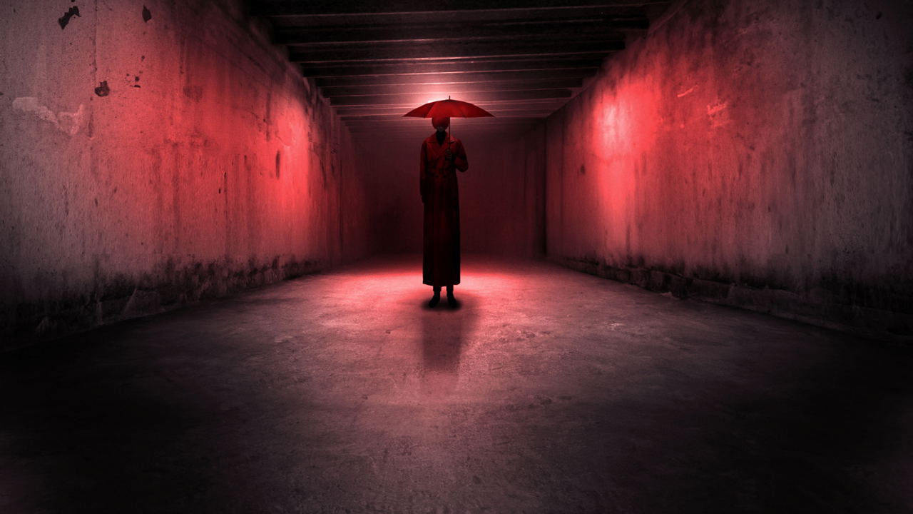 Person holding a red umbrella in a dark, narrow tunnel with red lighting.