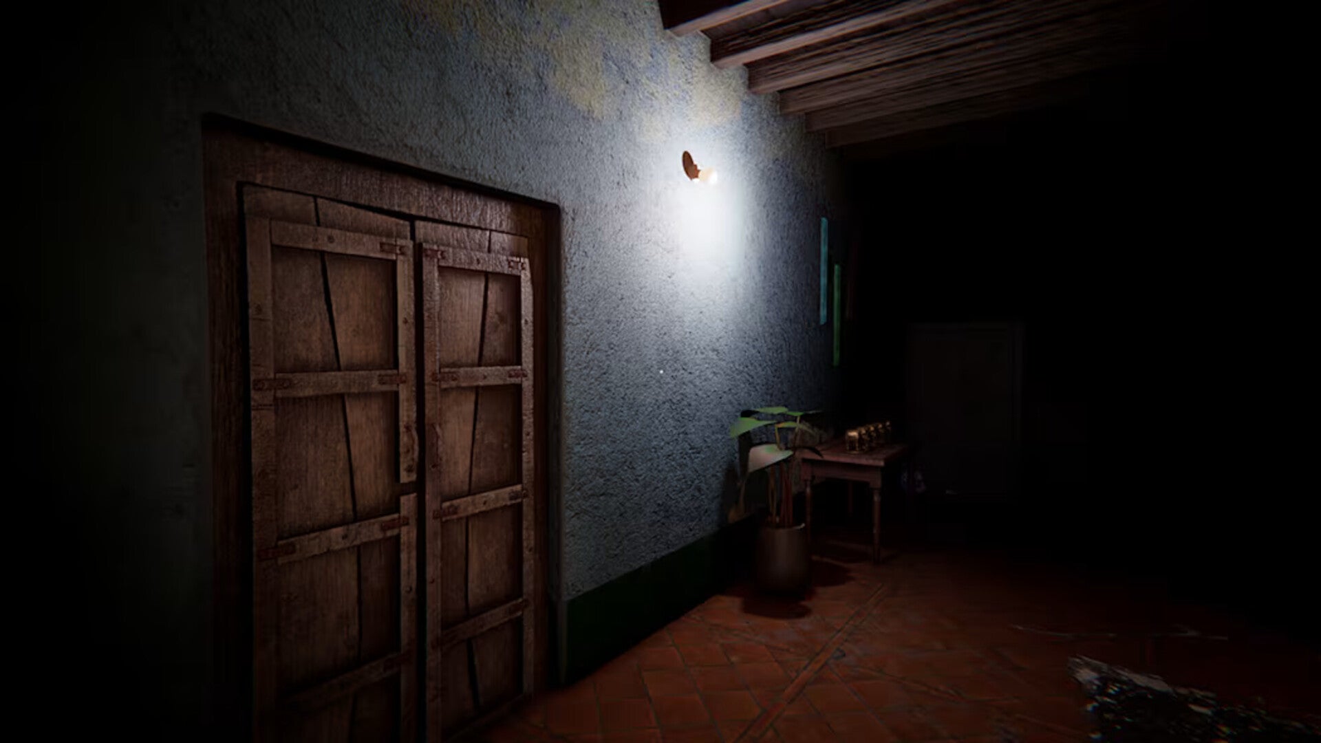 A dimly lit interior scene with a large wooden double door on the left, a textured gray wall with a small light source above, and a dark room extending to the right with a table and floor visible.