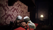 A dimly lit interior scene with two small doll-like characters seated on a red upholstered bench or bed against ornate burgundy damask wallpaper. A lit table lamp glows on the right, and the room is very dark overall.