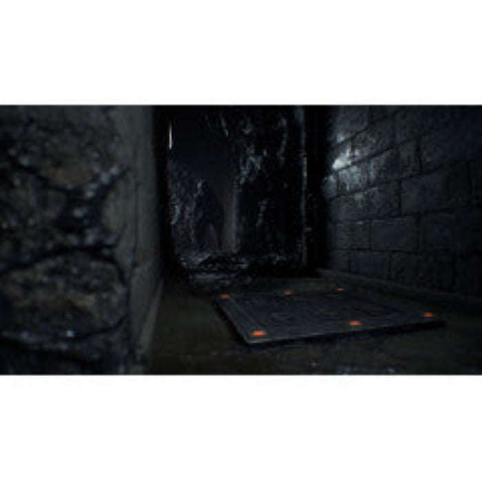 A dark, narrow stone corridor with a black rectangular floor mat or panel laid on the ground, shown in a dimly lit environment.