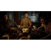 A dark, low-lit scene showing three people seated around a table in a dim interior, with a skull and candles on the tabletop.