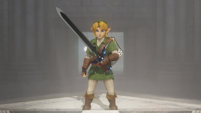 A collectible action figure of Link from The Legend of Zelda, standing on a light-colored platform in a misty gray environment. The figure is wearing his signature green tunic, white trousers, and brown boots, and holds a large sword over his shoulder.