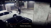 Person in a suit standing in a dimly lit garage with cars, timestamp and name displayed.