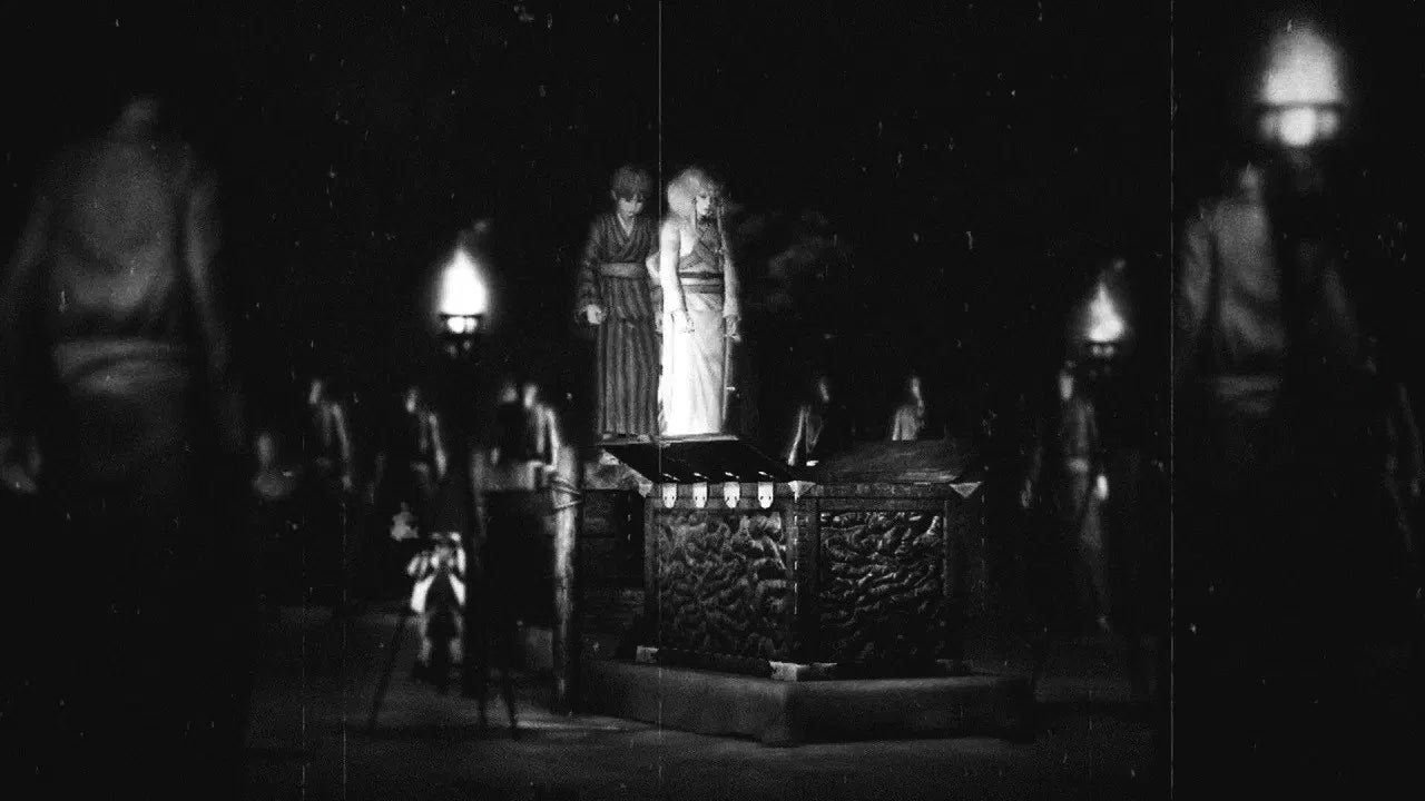 Black and white scene with statues and figures in a dark setting